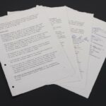 Quatre feuillets dactylographiés étalés en éventail sur fond noir, les deux de droite portant des signatures manuscrites en encre bleue