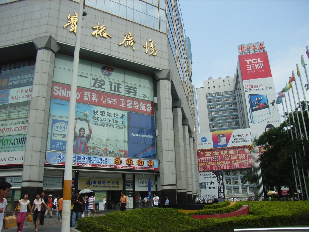 Façade de la SEG Plaza à Shenzhen, couverte d enseignes de marques informatiques, avec des passants chargés de cartons devant l entrée du marché électronique.