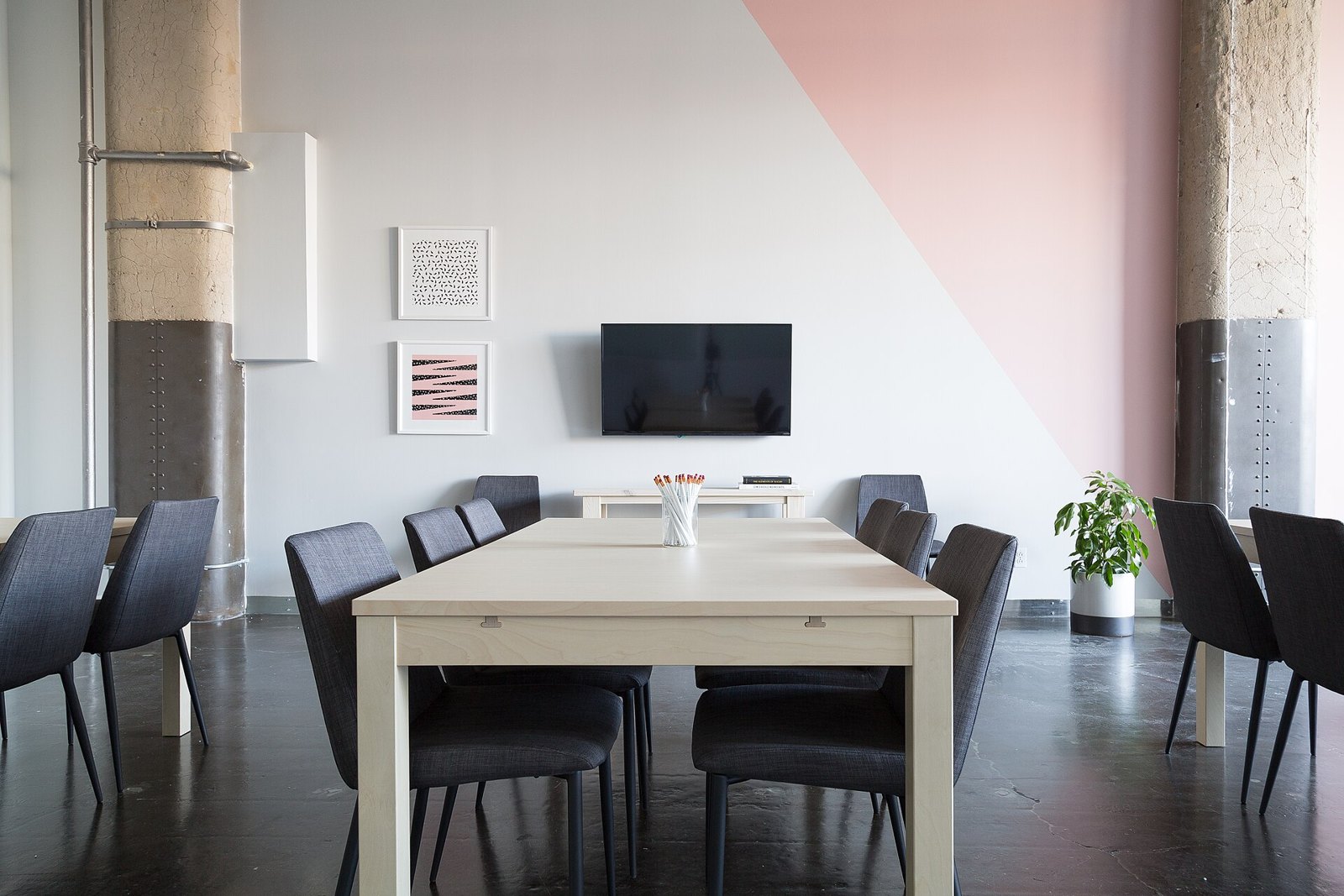 Une salle de réunion vide : une longue table claire, des chaises sombres repoussées, un écran éteint au mur.