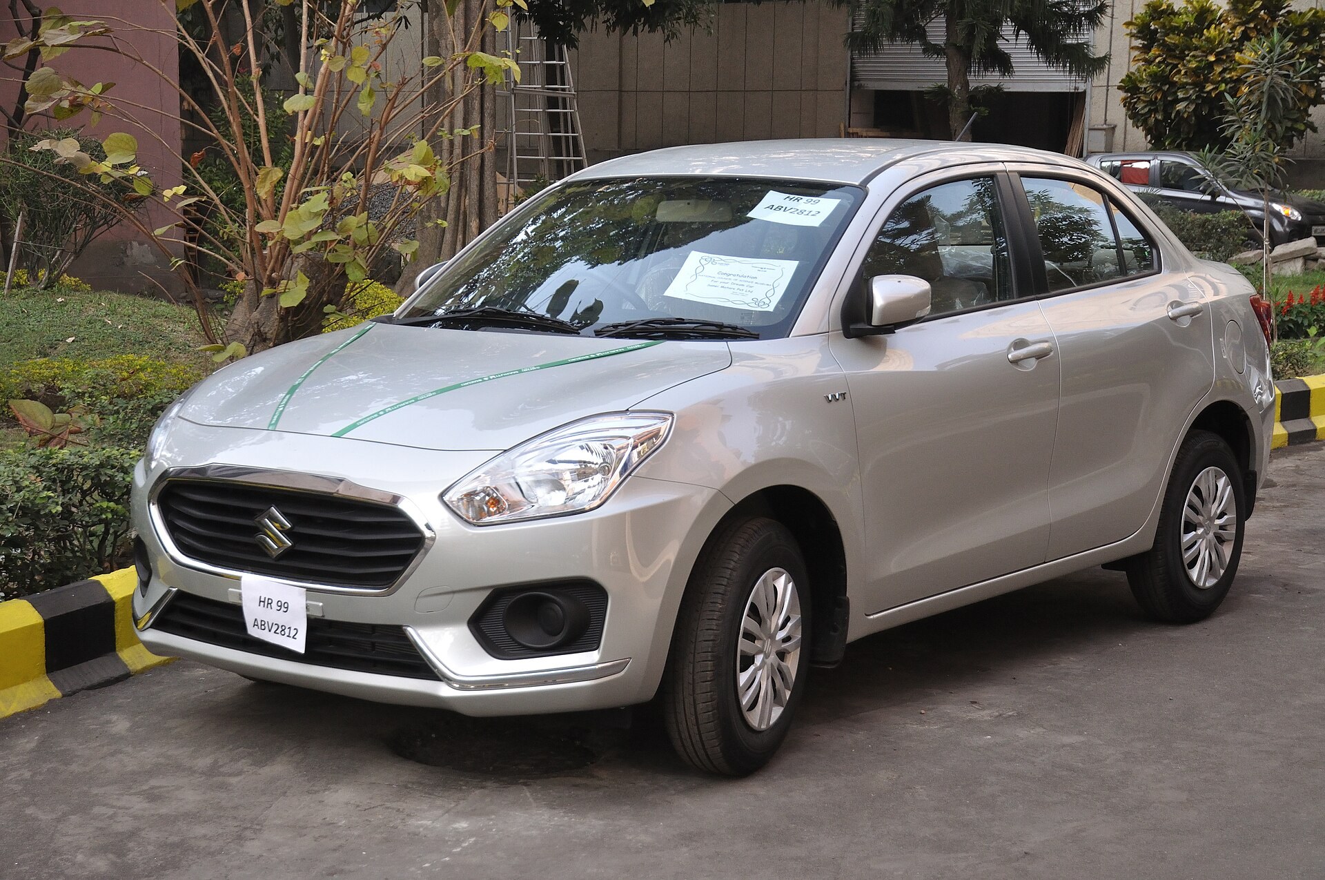 Une berline compacte Maruti Suzuki Dzire gris argent garee sur un parking.