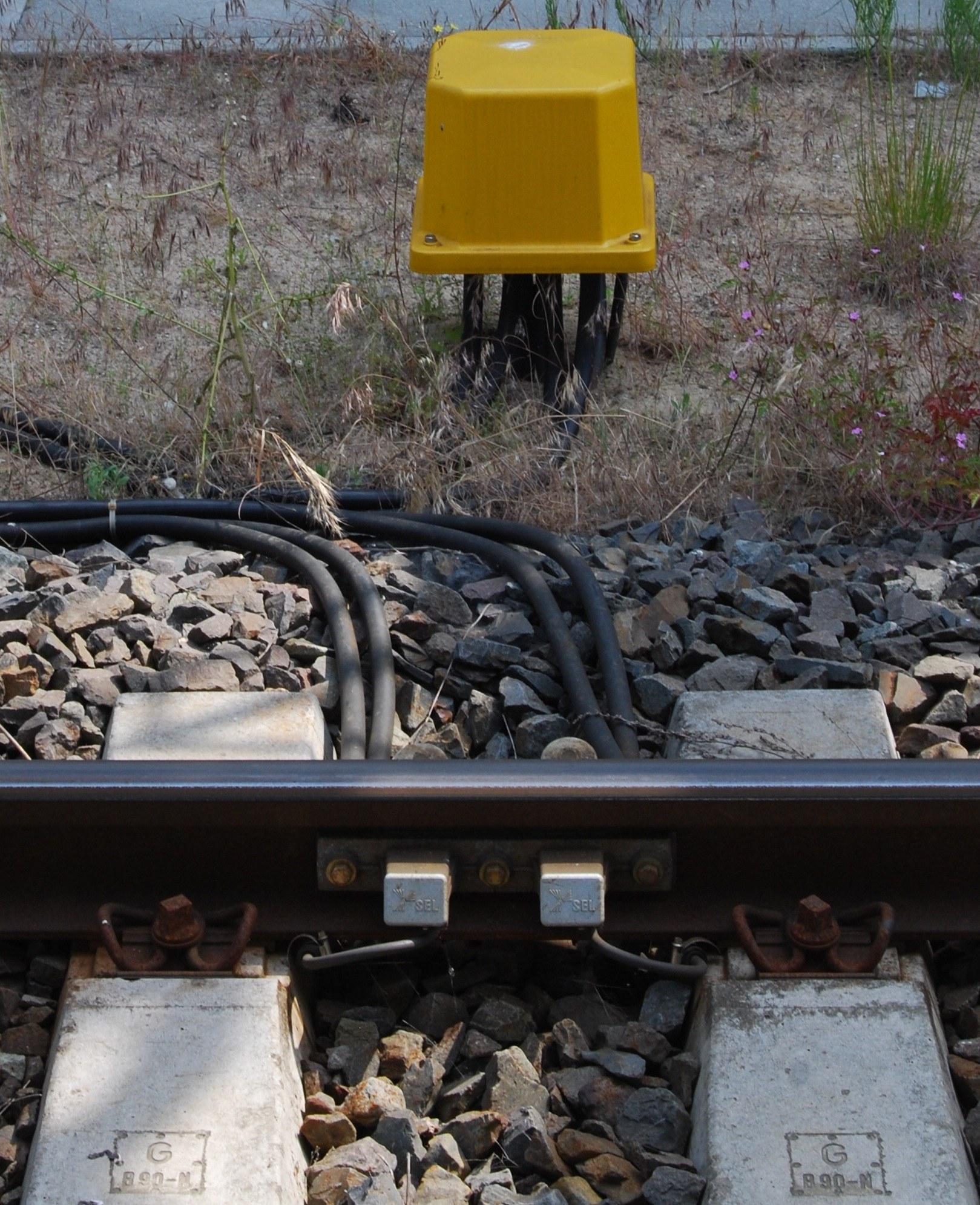 Un boitier jaune de signalisation ferroviaire pose le long d un rail.