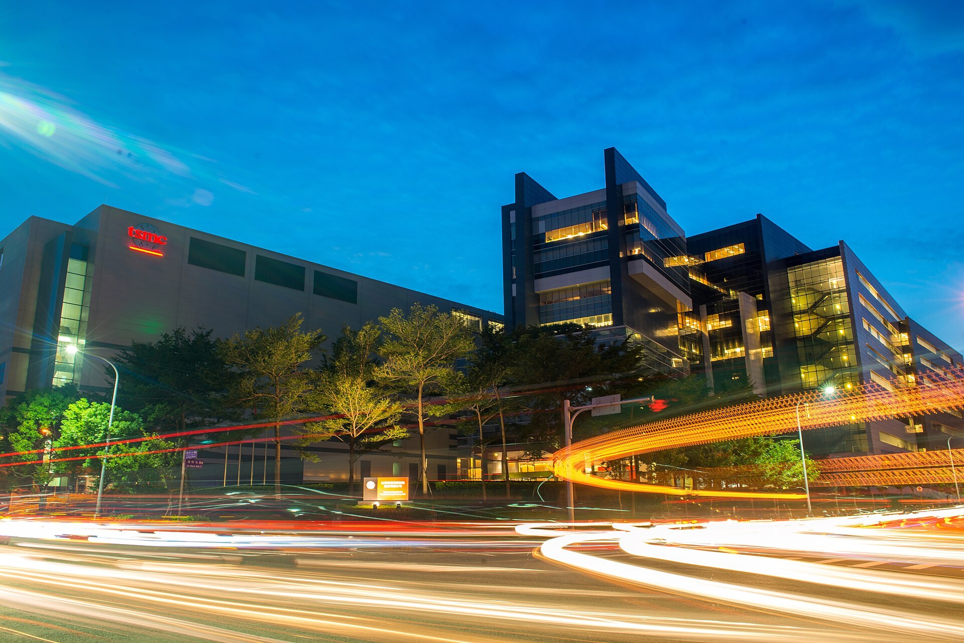 TSMC's Fab 12A lit up in the evening, behind a road with light trails.