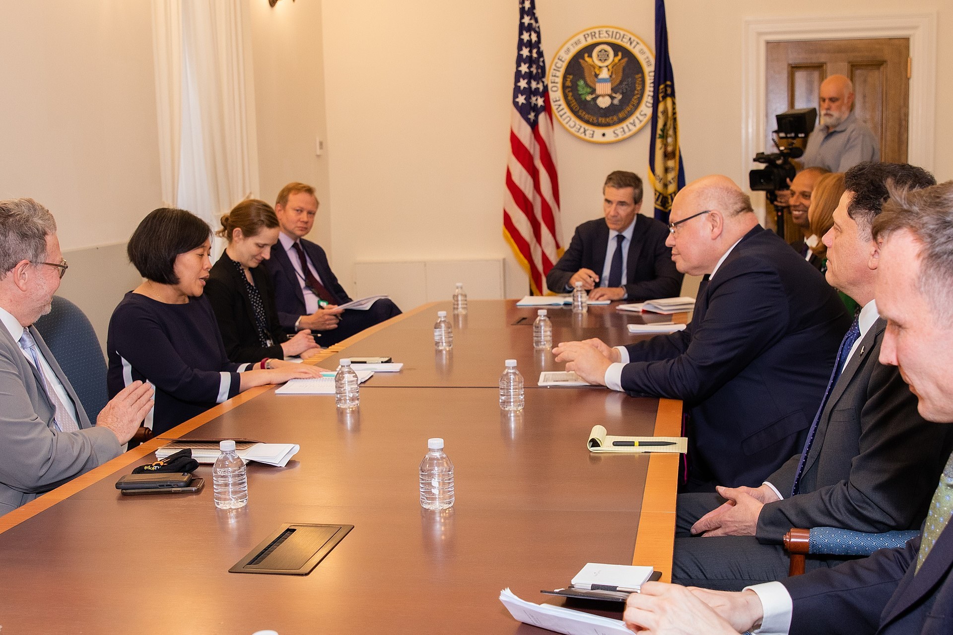 Deux delegations assises face a face a une longue table dans un bureau officiel americain.