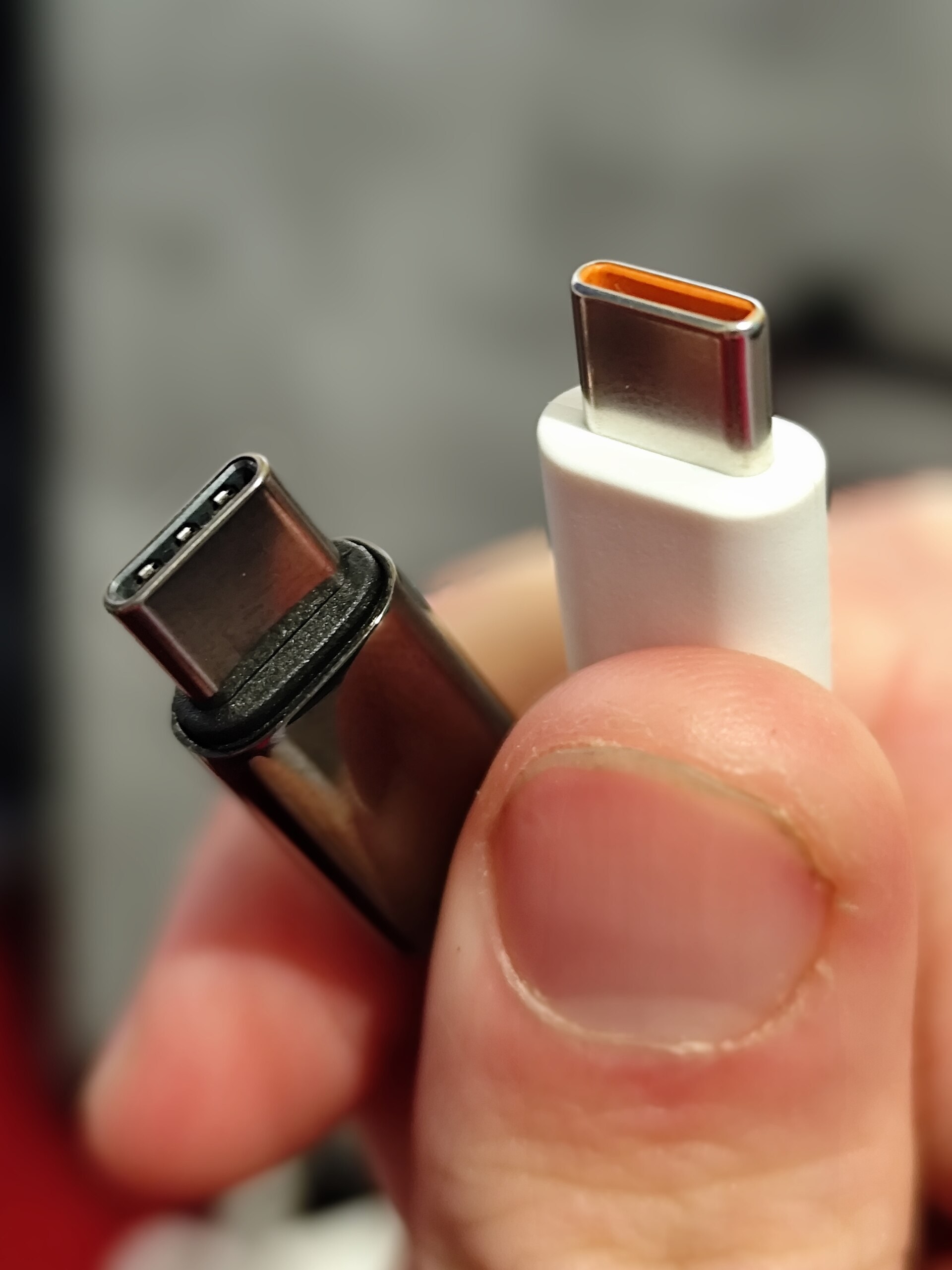 Une main tient deux fiches USB-C, l une noire, l autre blanche.
