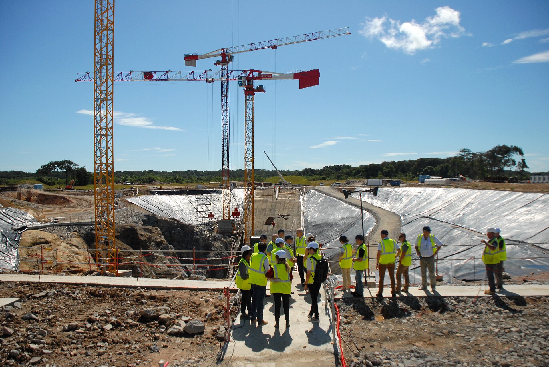Grues et fondations de beton sur le chantier du pas de tir d Ariane 6, des visiteurs en gilet jaune au premier plan.