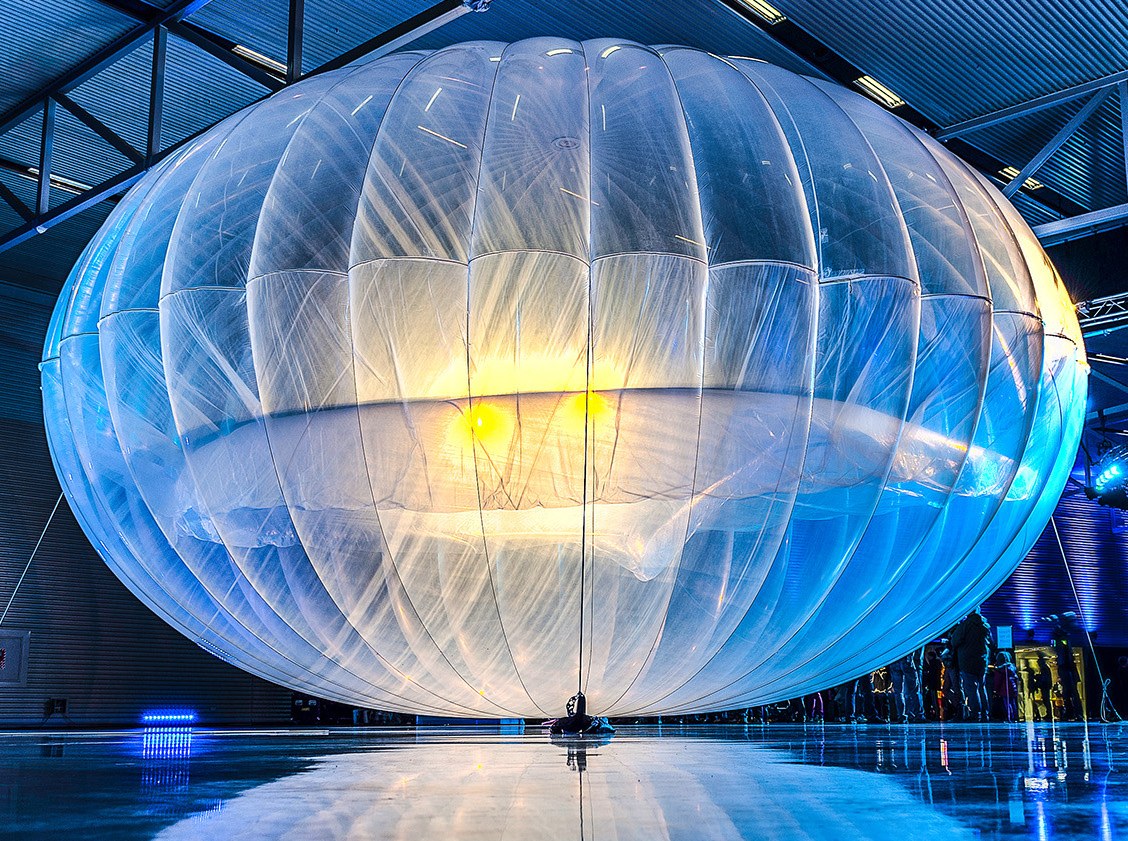 Un grand ballon translucide de Loon, gonfle et eclaire, expose dans un hangar.