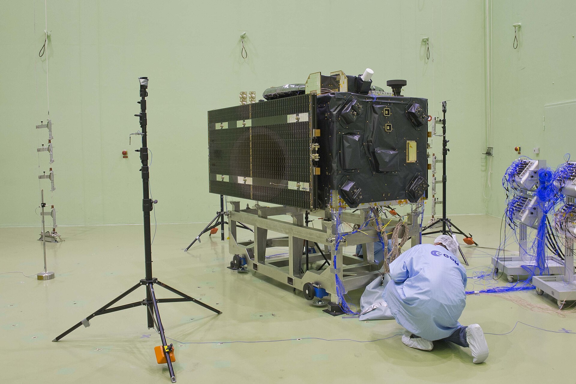 Un satellite Galileo en essai acoustique dans une grande salle blanche, entoure de micros sur pied.