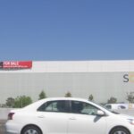 Le bâtiment de Solyndra à Fremont, en Californie, vu depuis l'autoroute, avec un panneau « for sale » posé sur la façade et l'enseigne de l'entreprise encore en place