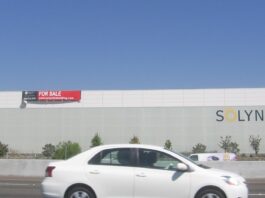 When the state steps back, the risk lands on your balance sheet Le bâtiment de Solyndra à Fremont, en Californie, vu depuis l'autoroute, avec un panneau « for sale » posé sur la façade et l'enseigne de l'entreprise encore en place